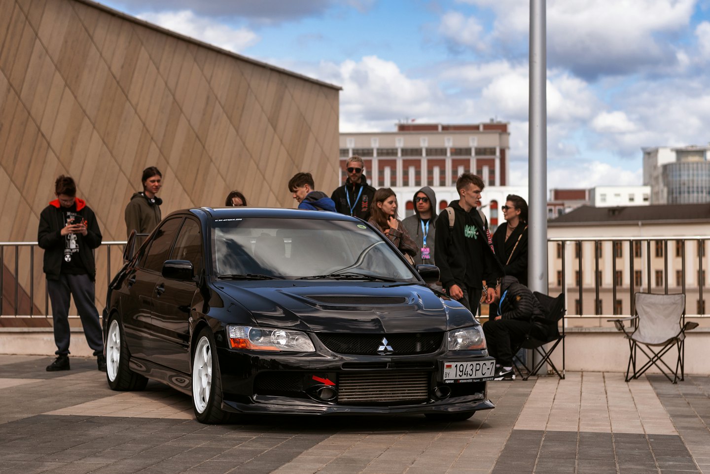 Friends gather around a modified black sedan at a car meet.