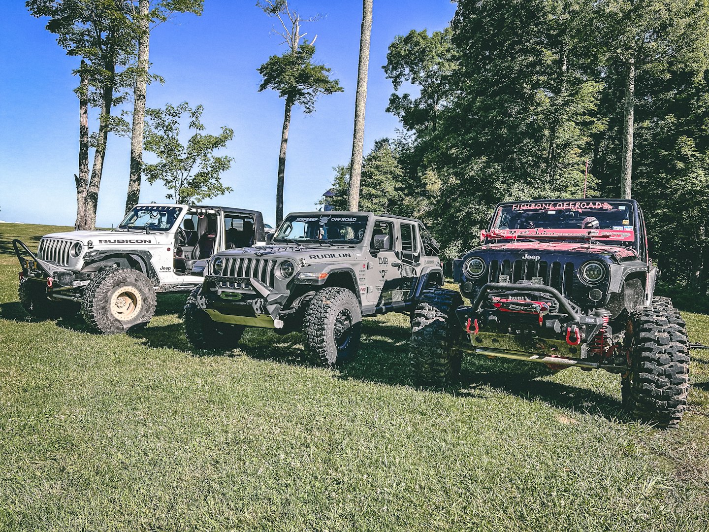 Three modified off-road Jeep Wranglers parked in a grassy field.