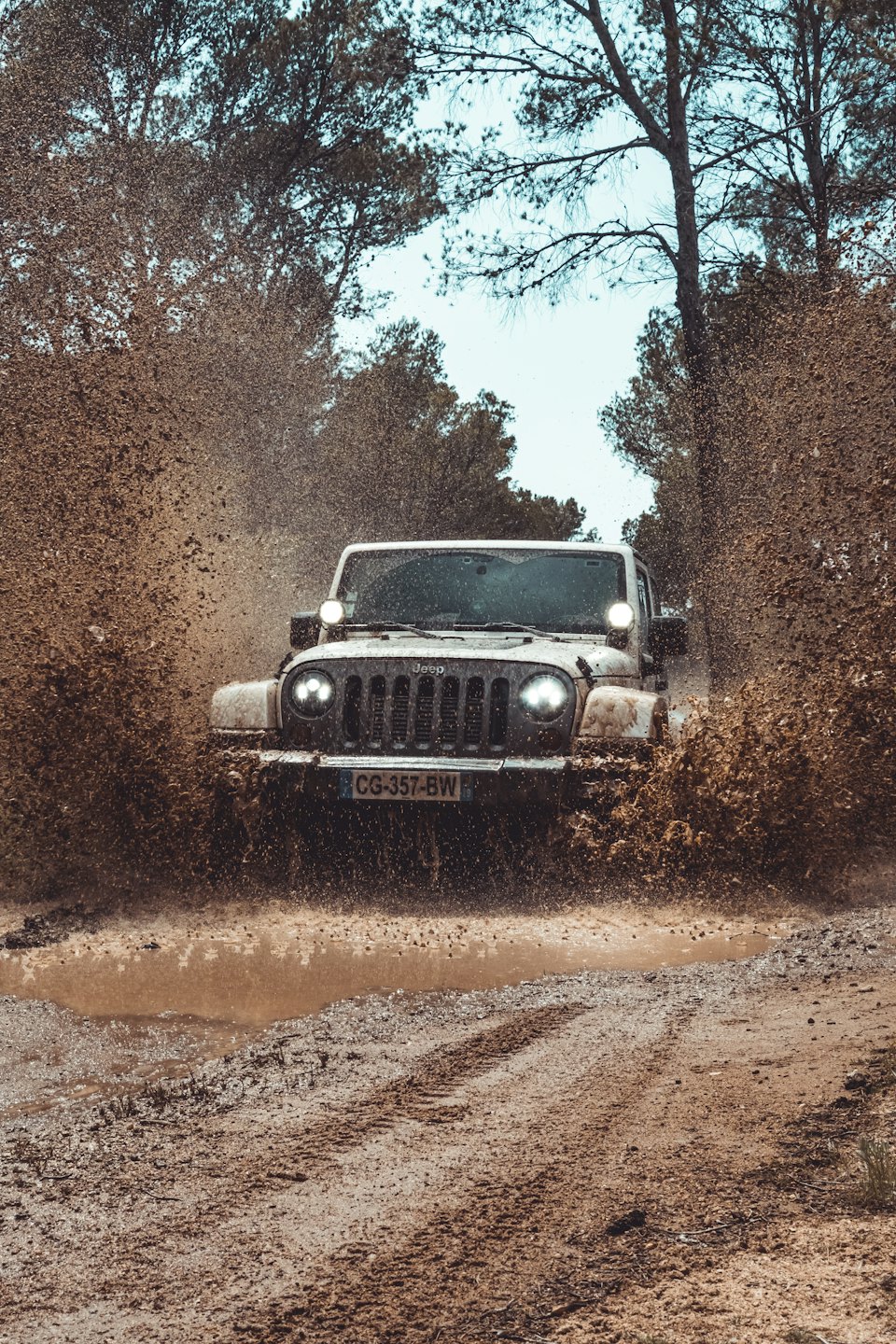 White off-road vehicle driving through a large mud puddle.