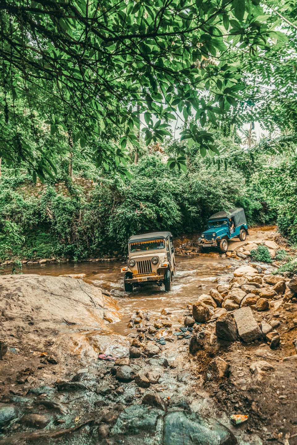 Two vintage jeeps drive through a muddy river.